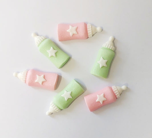 Six edible fondant icing baby bottle cake decorations in pink and mint colours with white stars on them.