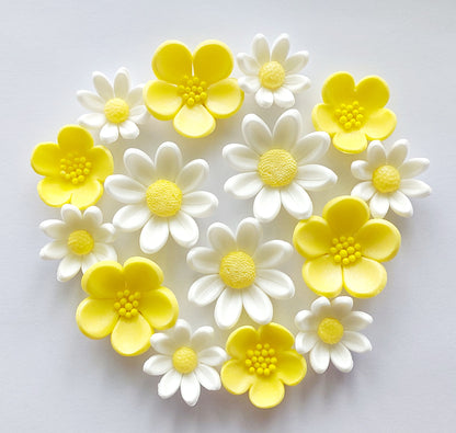 A collection of fondant icing flowers, with yellow and white petals, designed to look like buttercups and daisies.