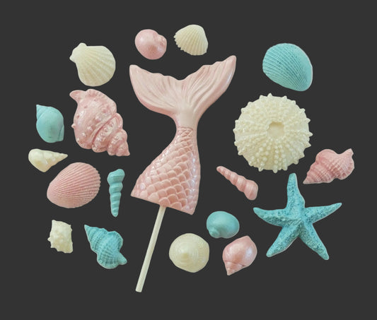 Pink mermaid tail lollipop surrounded by colorful shells, edible chocolate cake decorations